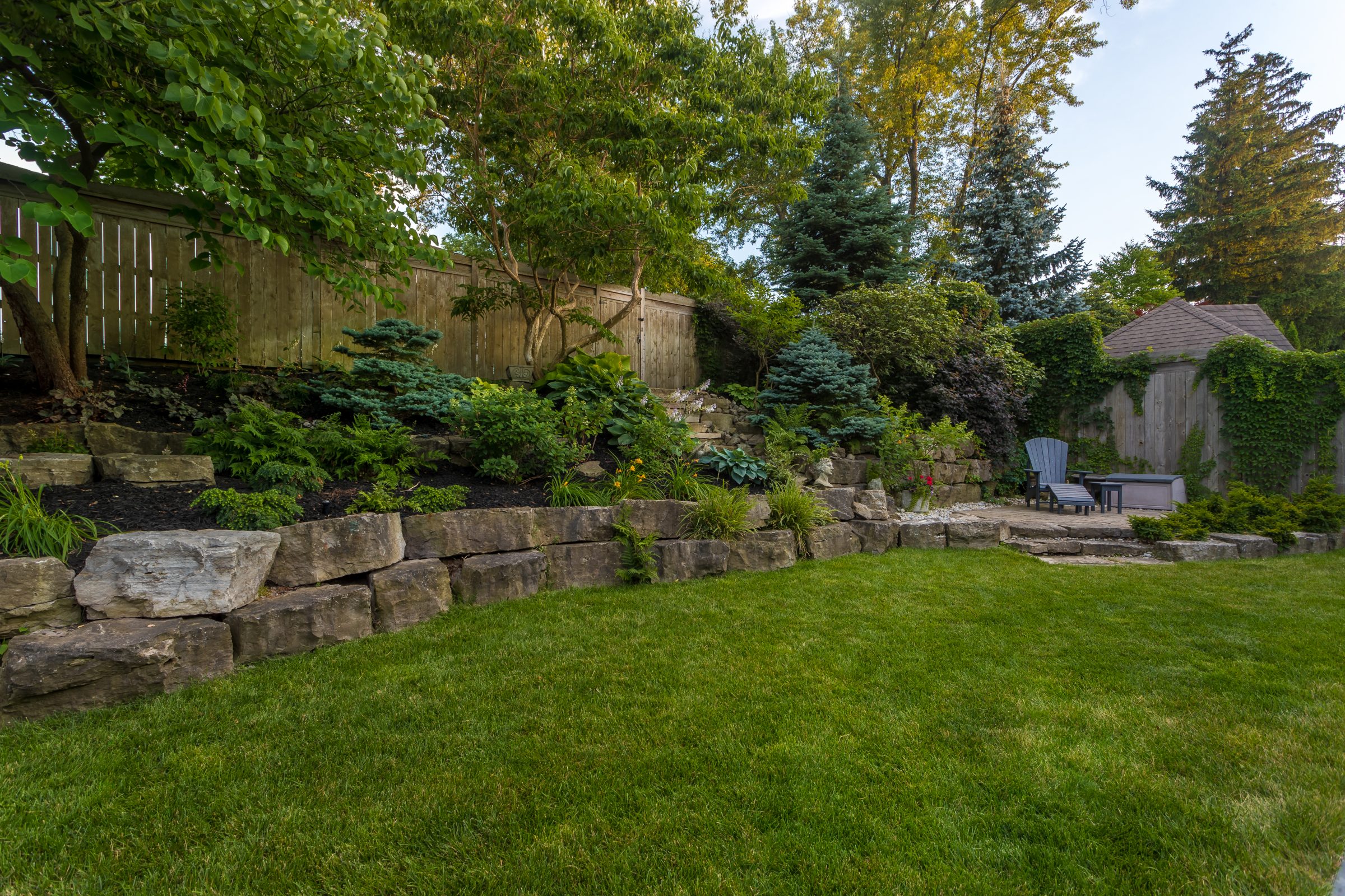 Lush backyard with stone wall and garden seating.