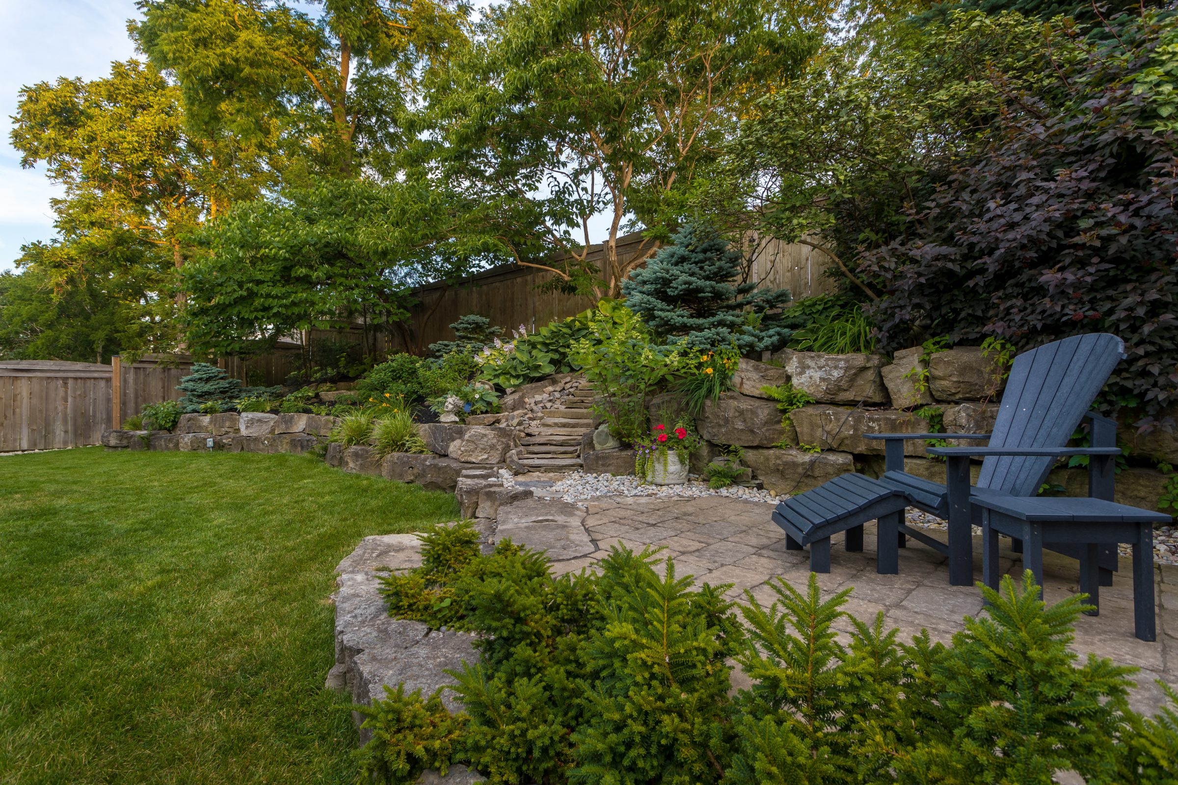 Backyard garden with patio chairs and stone pathway.