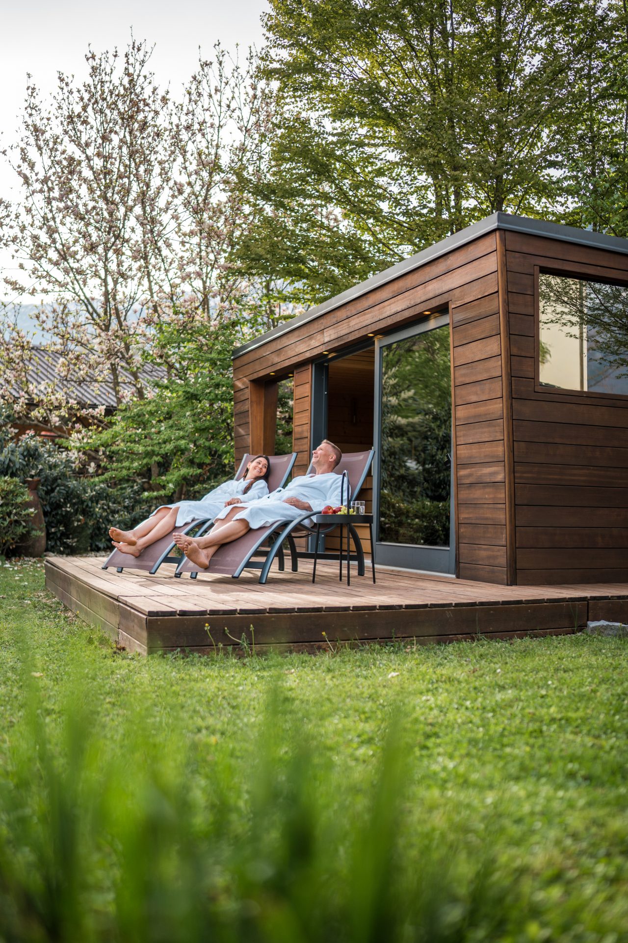 Couple relaxing on deck chairs by wooden cabin.